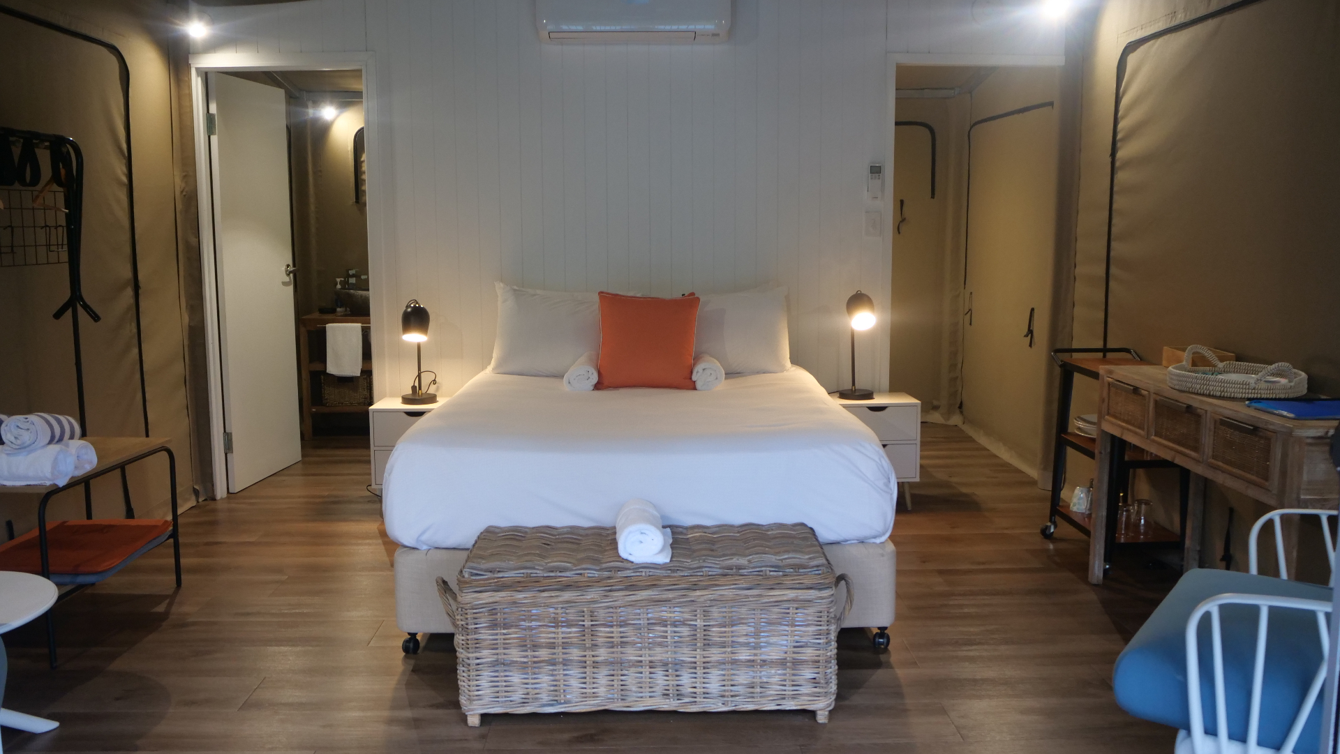 King bed with white linen and orange cushion accent, Magnetic Glamping